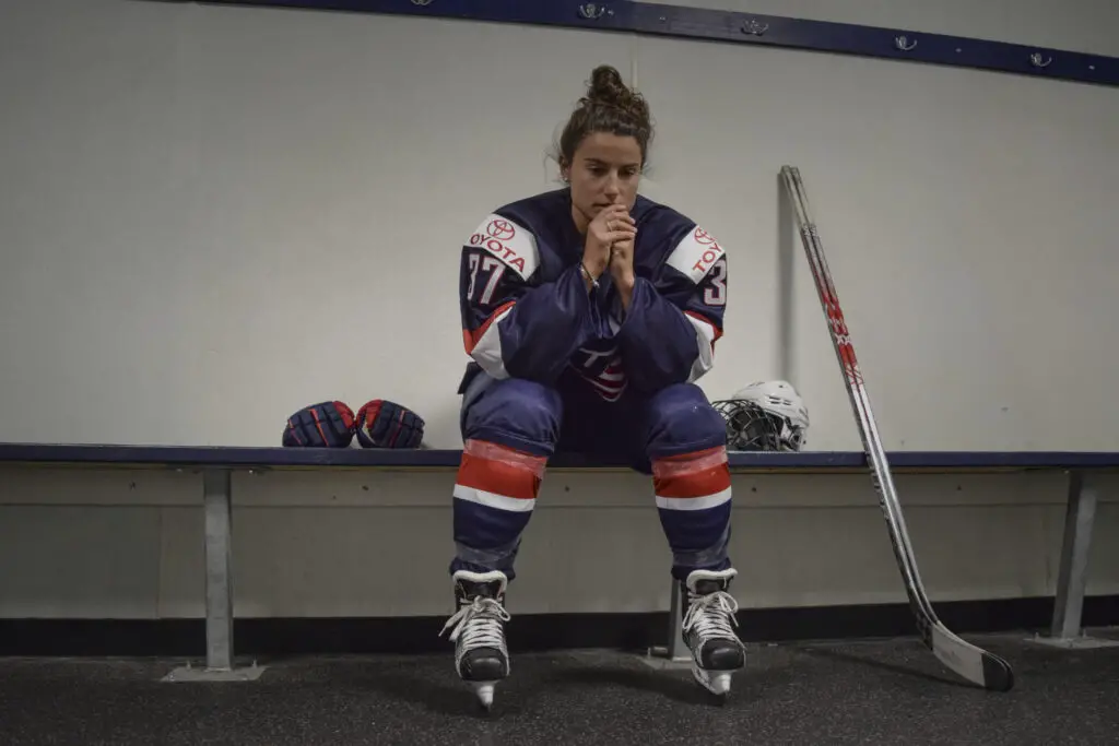 Amanda Pelkey sits on a bench dressed in her Team USA hockey gear. 